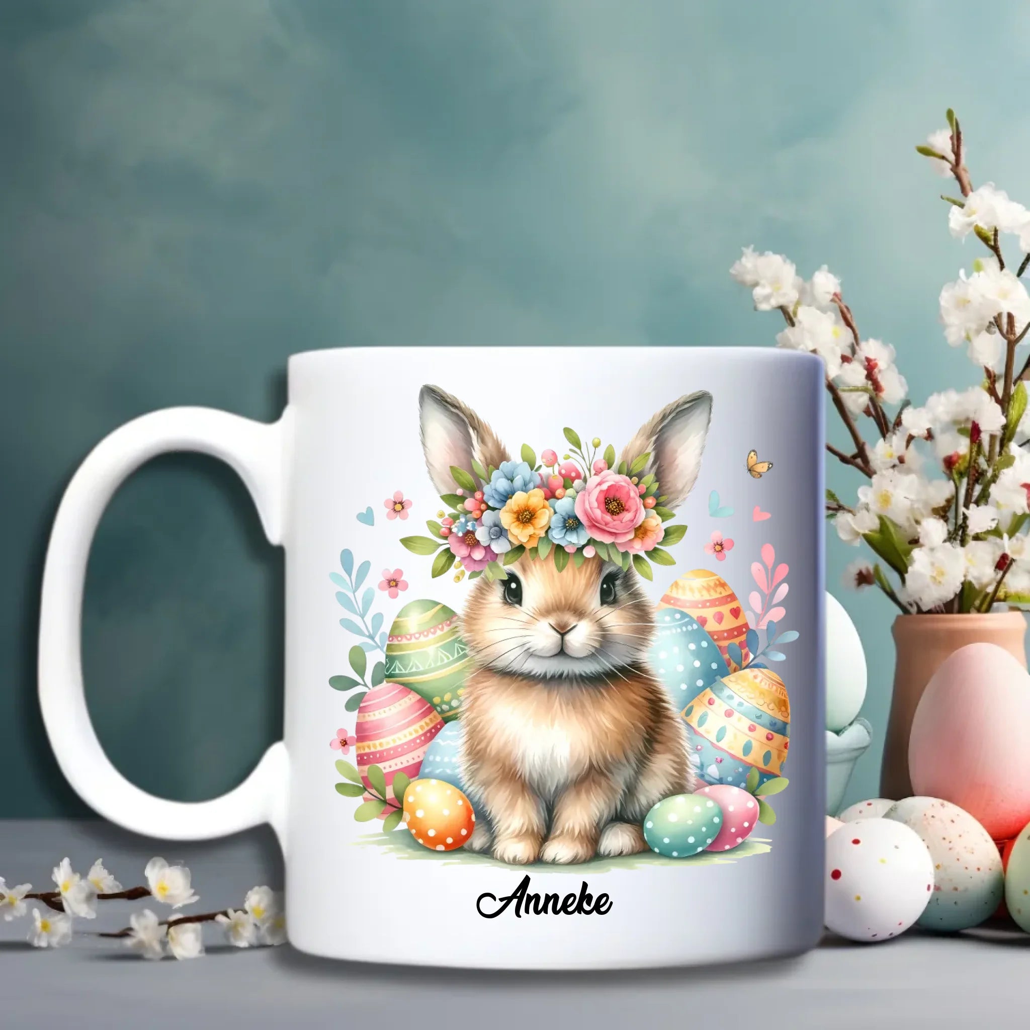 Witte keramische paasbeker met illustratie van haasjes tussen kleurrijke bloemen en optie voor personalisatie met naam - Debekershop.nl